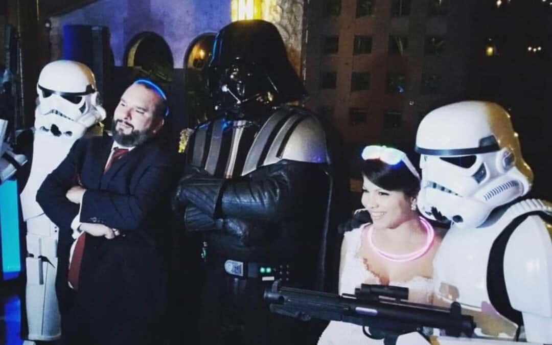 A bride and groom pose with people in Darth Vader and Stormtrooper costumes at a themed event.