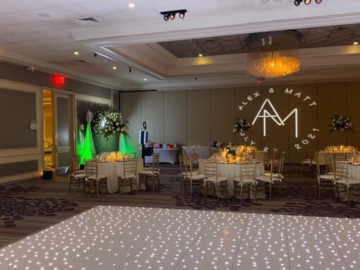 A dimly lit room with tables and chairs and a dance floor, set up for a wedding reception.