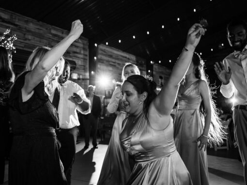 People dancing energetically at a formal indoor event with string lights overhead in a rustic venue.